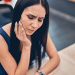 Young pretty woman holding cheek and suffering painful toothache
